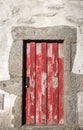 Red wooden aged door in stone wall. Ancient abandoned building. Medieval rustic architecture.