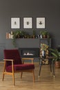 Red wooden armchair next to table with flowers in dark living room interior with posters. Real photo Royalty Free Stock Photo