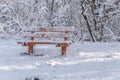 Red wooden bench covered with snow in the cold rural forest Royalty Free Stock Photo