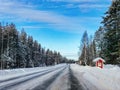 Red wooden bus stop covered by snow in winter countryside in Lapland Finland. Snow winter landscape with road and  forest Royalty Free Stock Photo