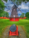 Red wooden cannon and a windmill in Kastellet fortress on a blue cloudy sky background