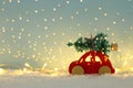 Red wooden car carrying a christmas tree over snow in front of blue background and golden garland lights. Royalty Free Stock Photo