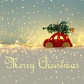 Red wooden car carrying a christmas tree over snow in front of blue background and golden garland lights. Royalty Free Stock Photo