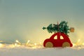 Red wooden car carrying a christmas tree over snow in front of blue background and golden garland lights. Royalty Free Stock Photo