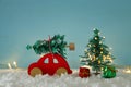 Red wooden car carrying a christmas tree over snow in front of blue background and golden garland lights. Royalty Free Stock Photo