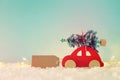 Red wooden car carrying a christmas tree over snow in front of blue background and golden garland lights. Royalty Free Stock Photo