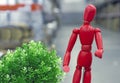 Red wooden doll Gestalta next to a green plant