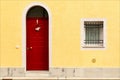 Red wooden door and window with bars on building facade with yellow wall.