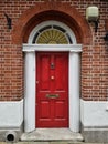 Red wooden front door with arch and pillars at a brick building.