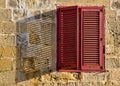 Red wooden louvered window with a shadow cast across the frame from the sunlight outside. Royalty Free Stock Photo