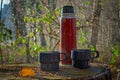 Red worn out thermos bottle with two blue cups