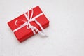 Red wrapped gift with a white ribbon on a woven, textured ecru backround. Royalty Free Stock Photo