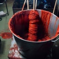 Red yarn dyeing process in metal buckets filled with vibrant red paint.