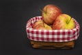 Red and yellow apples lie in a wicker wooden basket on a dark background, close-up, top view, checkered fabric. A place for your t