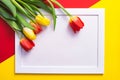 On a red-yellow background, white frame and red and yellow tulips lie Royalty Free Stock Photo