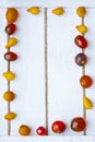 Red and yellow cherry tomatoes arranged in rectangular frame on white woos boards with rope, view from above. soft focus