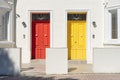 Red and yellow door side by side on white building facade, basking in sunlight. Royalty Free Stock Photo