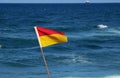 RED AND YELLOW LIFEGUARD FLAG WITH SEA IN BACKGROUND