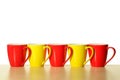Red and yellow mugs in a row on wooden table. White background Royalty Free Stock Photo