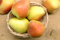 Red and yellow pears lays in wicker basket on brown wooden table top view closeup