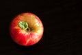 Red yellow ripe whole apple with green small leaf stands on a wooden dark brown table. Top view. Royalty Free Stock Photo