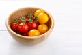 Red and yellow small cherry tomatoes in wooden bowl on white table Royalty Free Stock Photo