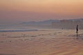 Sunset at the beach, a youg man standing on the water. Deserted beach with red sky far away