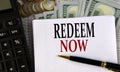 REDEEM NOW - words on a white sheet on the background of a calculator, coins and dollar bills