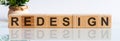 REDESIGN word concept written on wooden blocks, cubes on a white table with a flower and a light background