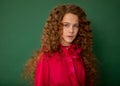 Redhair beautiful girl with curly afro curls in bright pink blouse on green background. Curly hair care, freckle cream, teen book