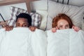 Redhaired ginger caucasian happy female and multi-ethnic afro man together lying in bed bedroom hiding under the blanket Royalty Free Stock Photo