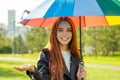 Redhaired ginger woman standing under colorful umbrella in summer park checking for rain rainbow