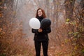 Redhaired girl in the autumn forest loughing and holding black and white balloon. The concept of choice, good and evil