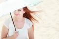 Redhaired girl sitting under umbrella on beach.