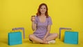 A redhaired woman sits crosslegged on the floor, holding a paper cup of coffee or tea. Young woman in summer clothes