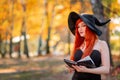 Redhead beautiful glamorous witch in black hat with magic book in hands