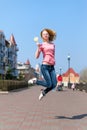Redhead beautiful young woman jumping high in air over blue sky holding colorful lollipop. Pretty girl having fun outdoors. Royalty Free Stock Photo