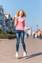 Redhead beautiful young woman jumping high in air over blue sky holding colorful lollipop. Pretty girl having fun outdoors. Royalty Free Stock Photo