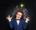 Redhead boy is is mischievous against blackboard background with lightbulb and question marks. Brainstorming and idea concept Royalty Free Stock Photo