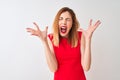 Redhead businesswoman wearing elegant red dress standing over isolated white background celebrating mad and crazy for success with