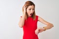 Redhead businesswoman wearing elegant red dress standing over isolated white background Looking at the watch time worried, afraid