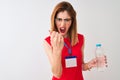 Redhead businesswoman wearing id card drinking water over isolated white background annoyed and frustrated shouting with anger, Royalty Free Stock Photo