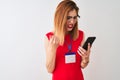 Redhead businesswoman wearing id card using smartphone over isolated white background annoyed and frustrated shouting with anger, Royalty Free Stock Photo