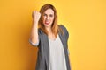 Redhead caucasian business woman over yellow isolated background Shouting frustrated with rage, hands trying to strangle, yelling