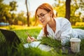 Female Copywriter makes notes while lying on the grass in natural park uses laptop pc. mobile office Royalty Free Stock Photo