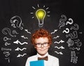 Redhead child boy with question and lightbulb on blackboard background