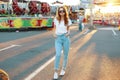 Redhead cute young hipster woman in stylish T-shirt in trendy sunglasses in blue jeans poses in an amusement park Royalty Free Stock Photo