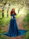 Redhead fantasy woman queen. Blue long velvet medieval dress, vintage clothing. Red curly hair flying waving in wind