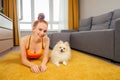 Redhead ginger girl lying down with white small dog spitz on the carpet and looking at camera