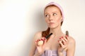 Redhead girl with clean skin in a towel and bandage on her head with a mirror and a brush in her hands looks up